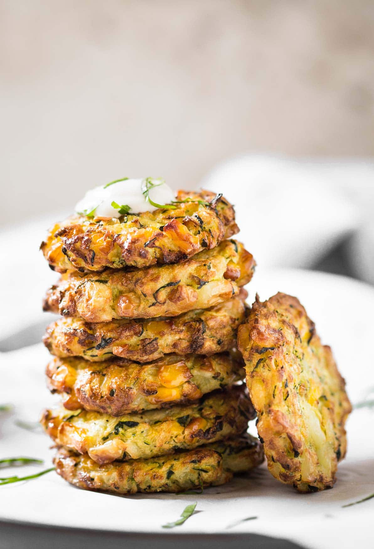 Air fryer zucchini corn fritters are stacked on a white plate