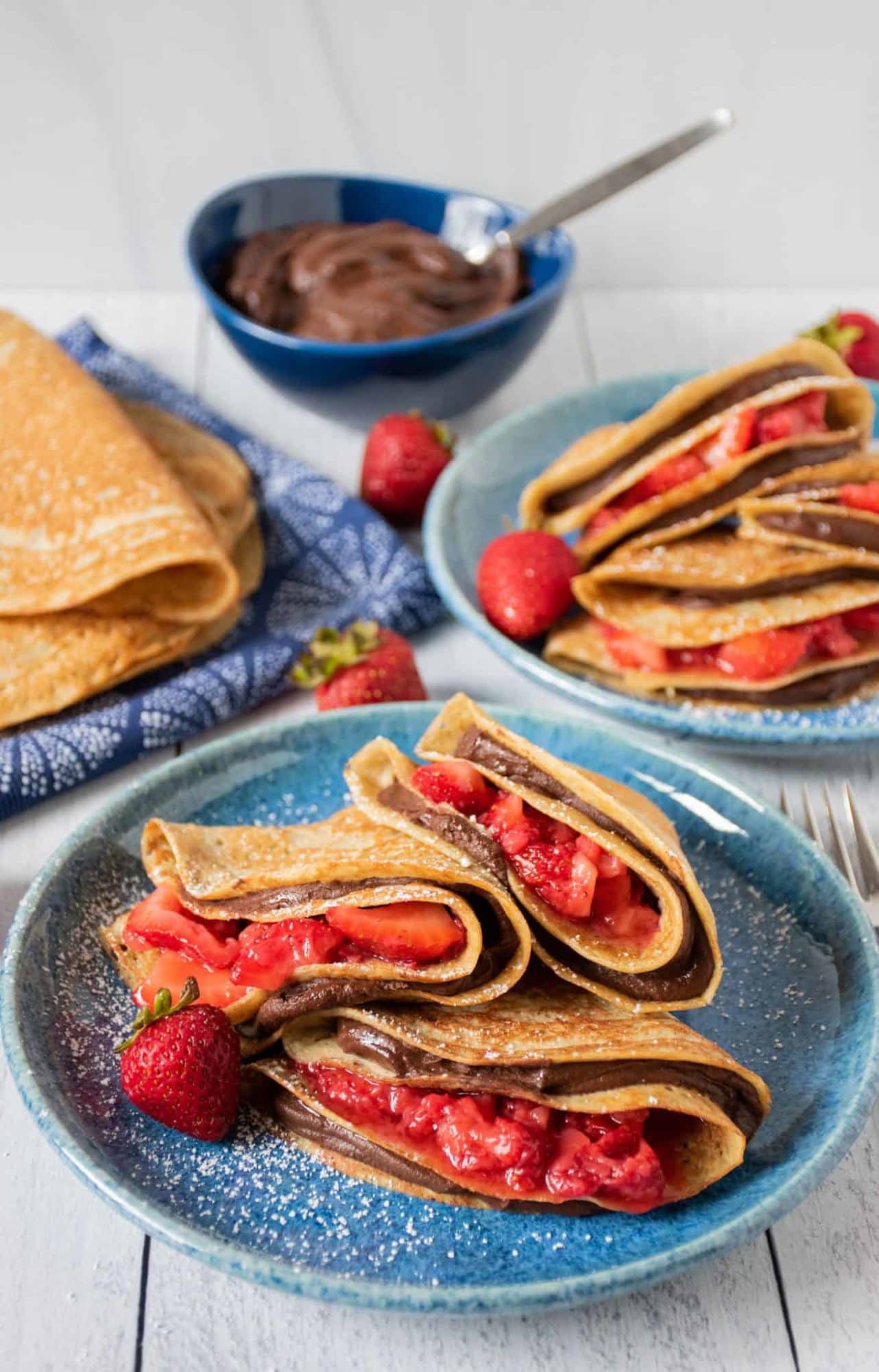 Plates of healthy crepes filled with brownie batter and sliced strawberries
