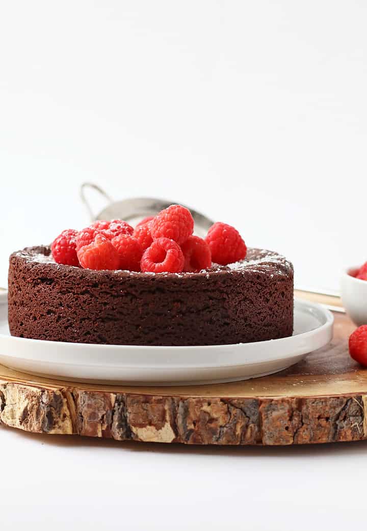 A vegan flourless chocolate cake made using a garbanzo bean flour recipe is topped with raspberries