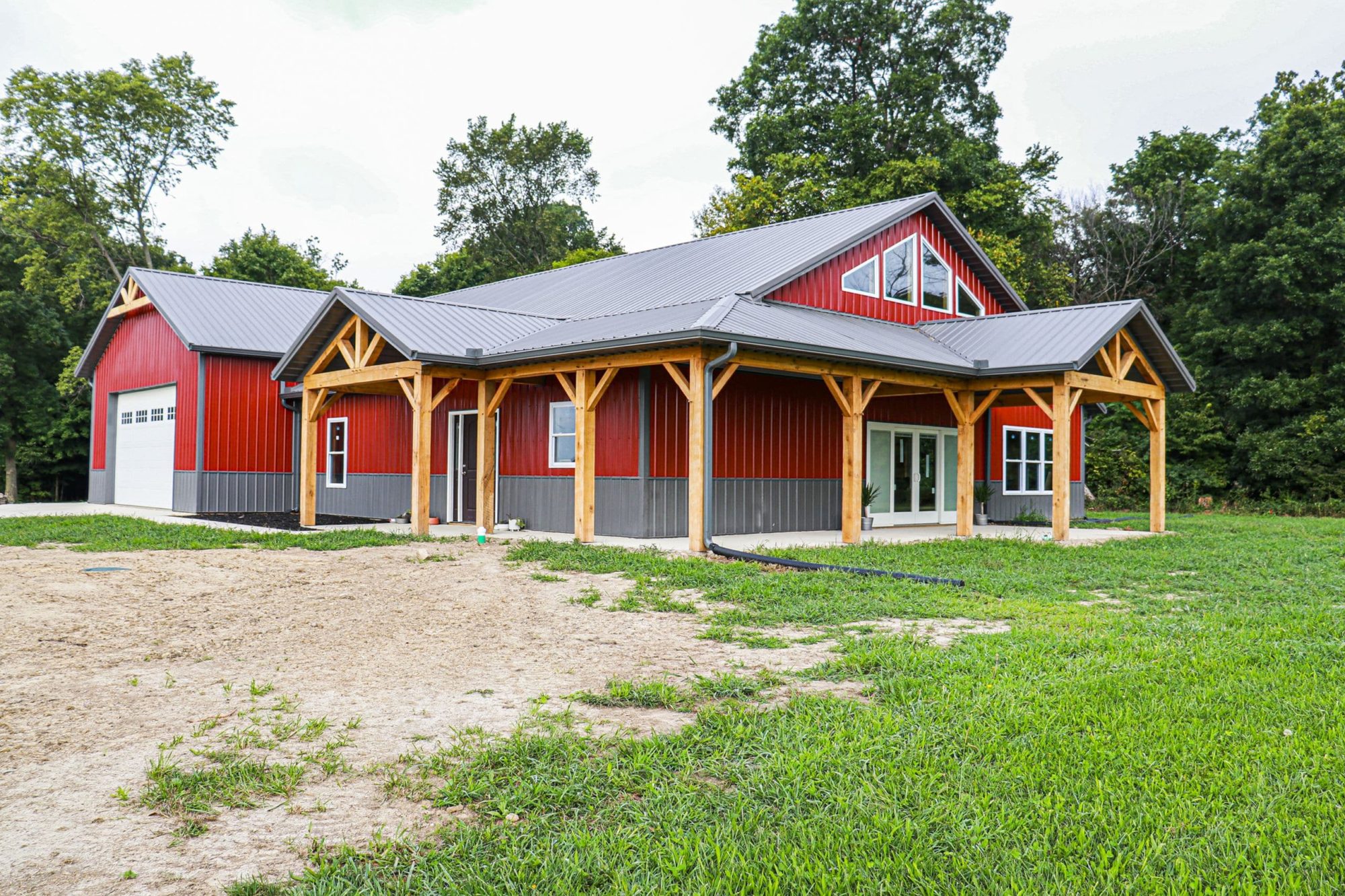 A red pole barn house with wrap around porch and decorative wood beams