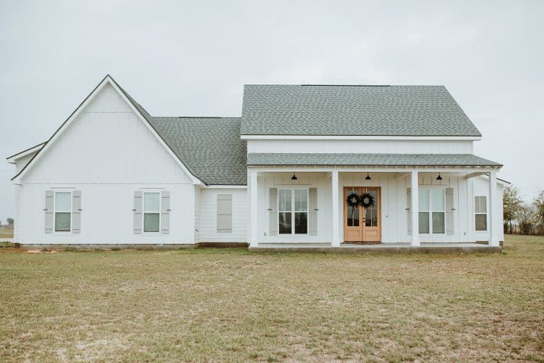 A white barndominium house with double front doors and a long porch